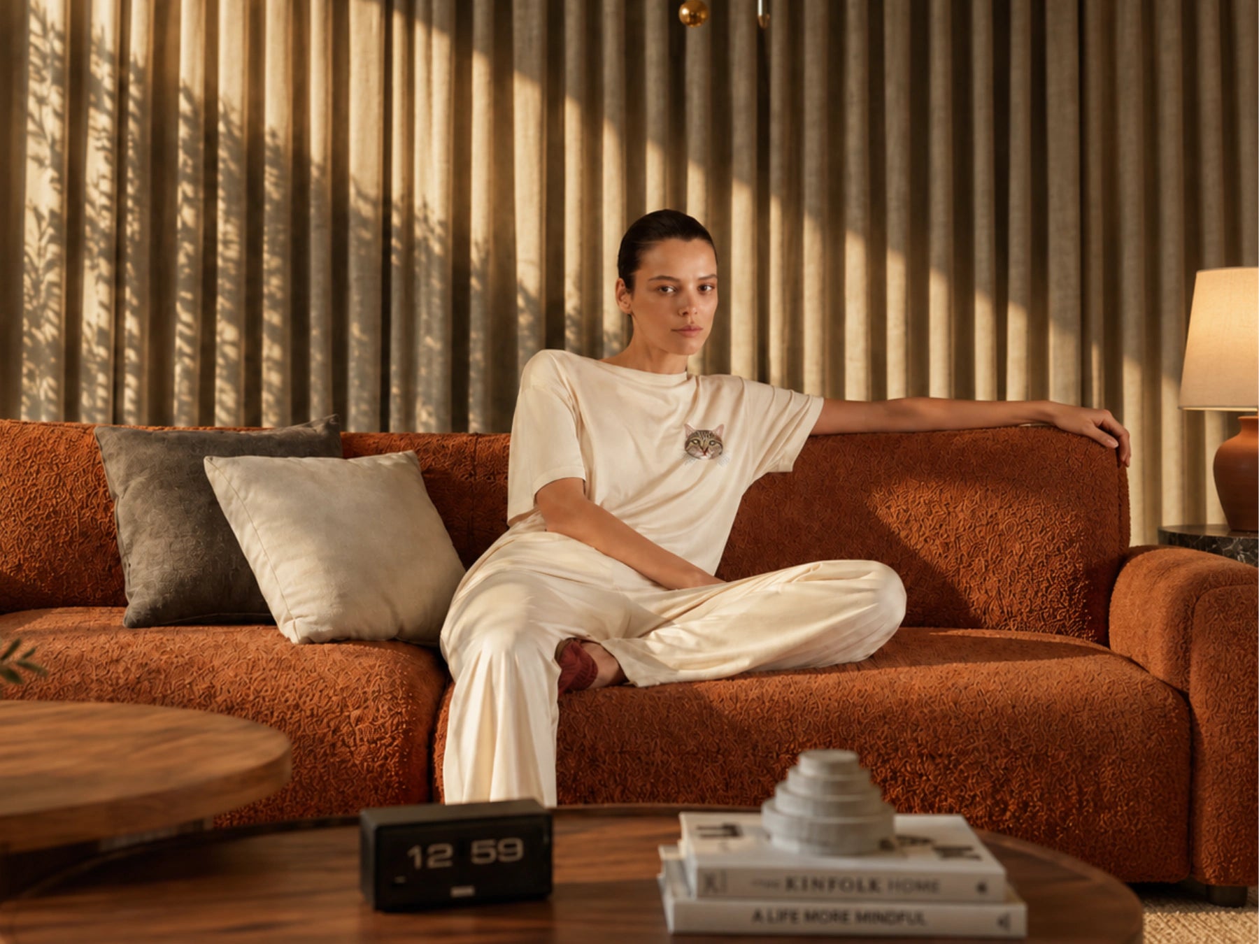 A woman wearing a cream cat-portrait T-shirt on a warm brown sofa
